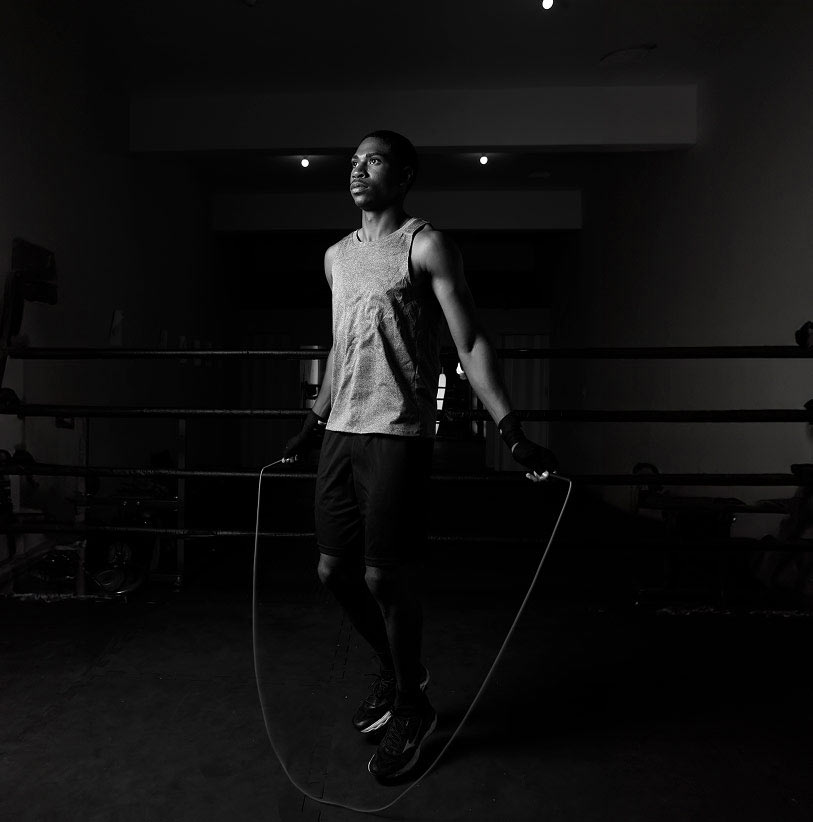 Foto preto e branco com um homem negro de regata dentro de um ringue pulando corda